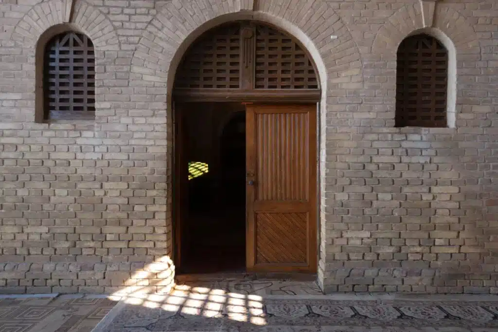 Interior with geometric light patterns cast through wooden lattice shutters onto a polished floor