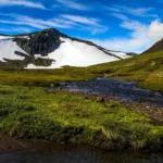 Arktisk landskap vid solnedgång med skogsbevuxen terräng, älv och snöklädda fjäll i gyllene ljus